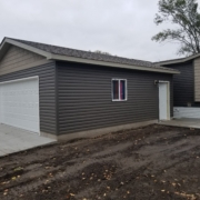 new home addition with a white garage door and dark grey siding - Barefoot Construction Deck Construction, Basement Finishings and Home Additions