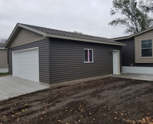new home addition with a white garage door and dark grey siding - Barefoot Construction Deck Construction, Basement Finishings and Home Additions