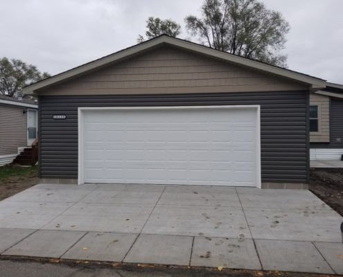 new home addition with a white garage door and dark grey siding - Barefoot Construction Deck Construction, Basement Finishings and Home Additions