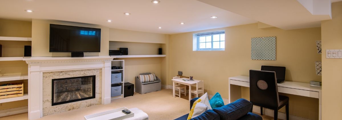 finished basement with a fireplace and blue couch - Barefoot Construction basement finishing