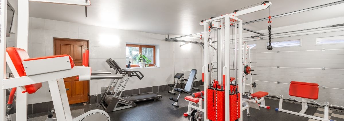 home gym located in the basement with white and red equipment - Barefoot Construction basement finishing