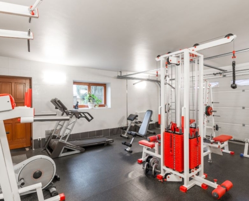 home gym located in the basement with white and red equipment - Barefoot Construction basement finishing